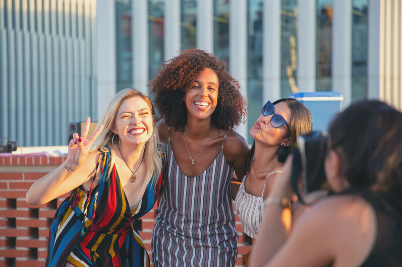 Anonymous woman photographing positive diverse ladies during event on rooftop